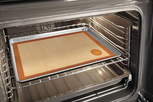Large non-stick silicone baking mat with brown trim placed on a metal baking sheet inside an oven, designed for durability in Kitchen & Food, Cookware, Baking Supplies, and Best Sellers collections.