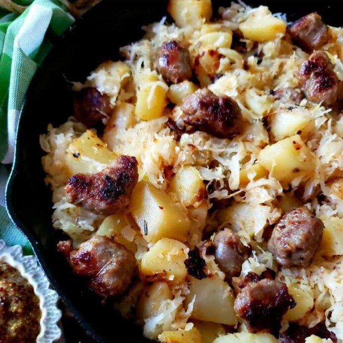 Cast iron skillet filled with a hearty mixture of browned sausage pieces, roasted potatoes, and sauerkraut, styled for Kitchen & Food, Food, Pantry, USA Made, Best Sellers, and Promo Eligible collections.