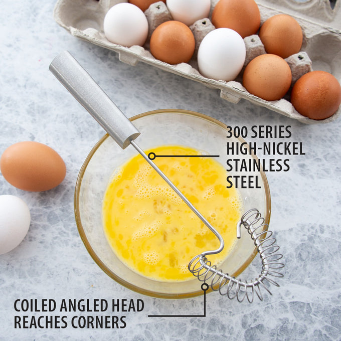 Stainless steel coil whisk with angled head designed to reach pan corners, shown whisking beaten eggs next to carton of brown and white eggs, part of Kitchen & Food and USA Made collections.