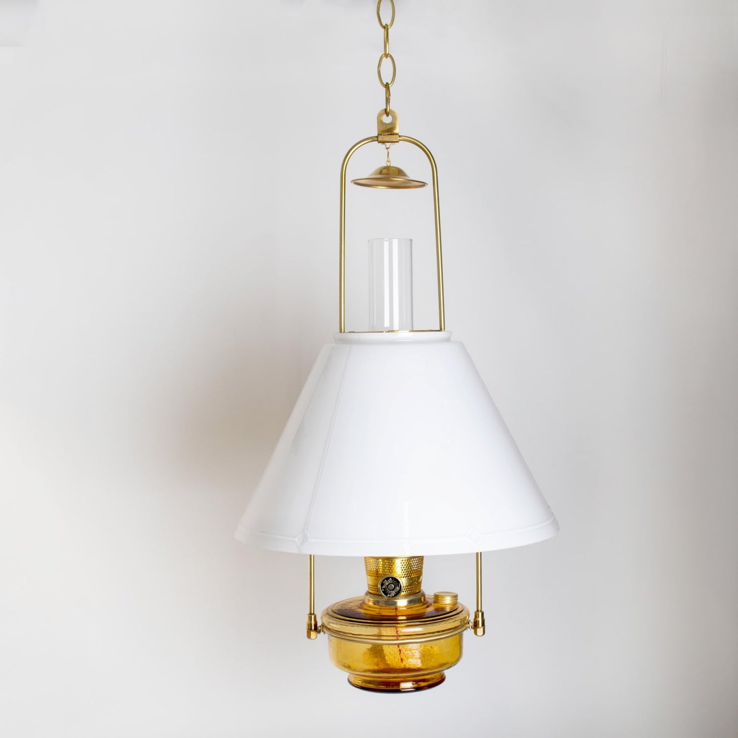 Handcrafted amber glass hanging oil lamp with brass tilt-frame, featuring white conical shade, ideal for lamps & lighting, farm, garden, and best sellers collections.