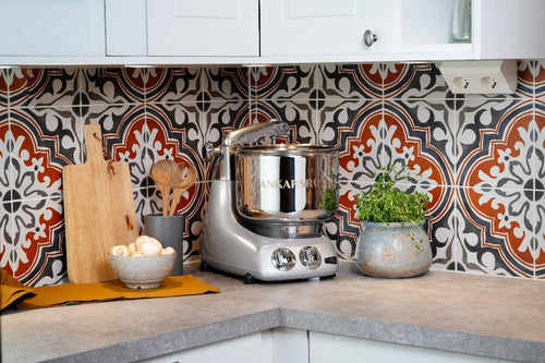 Silver stand mixer with polished steel bowl placed on a kitchen countertop, accompanied by wooden cutting boards, fresh mushrooms in a bowl, and a potted herb, suitable for Kitchen & Food and Baking Supplies collections.