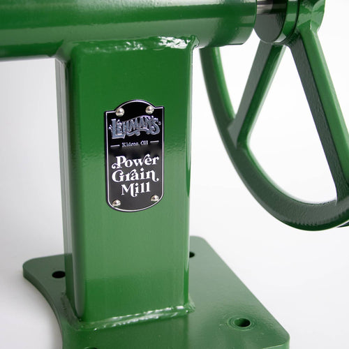 Close-up of green heavy-duty grain mill base with attached hand crank, featuring a metal label marked with brand and model, suitable for homesteading and emergency supplies collections.