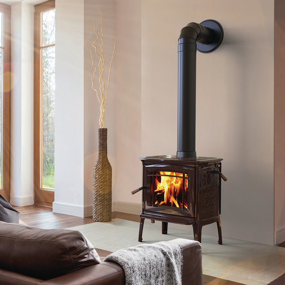 Cozy living room featuring a handcrafted Hearthstone Crafts wood stove with visible flame, black pipe vent, set against a neutral wall near a tall window and woven decor, part of best-selling heatstoves collection.