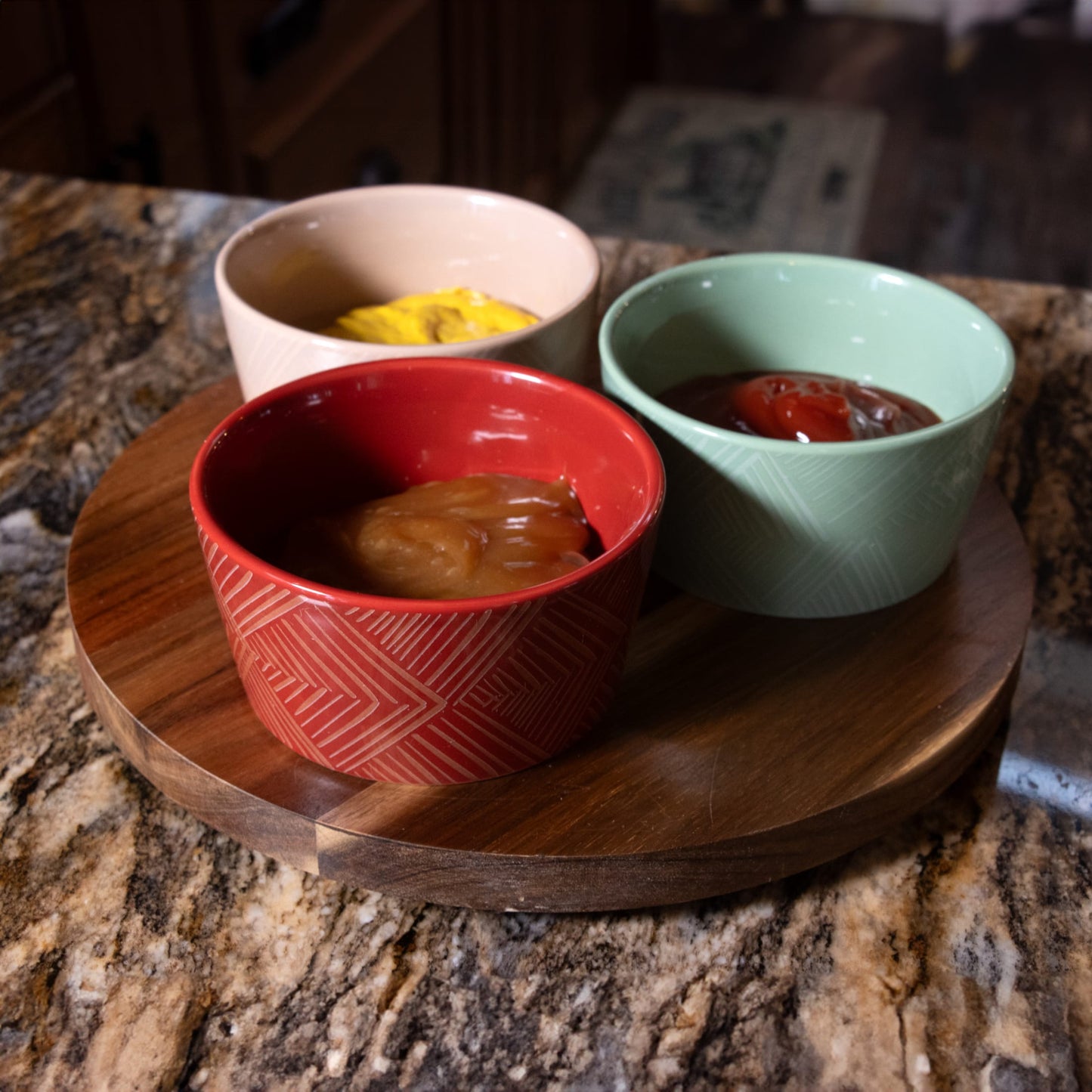 Round wooden turntable with three ceramic condiment bowls in red, beige, and green holding ketchup, mustard, and barbecue sauce, designed for easy serving in Kitchen & Food collections.