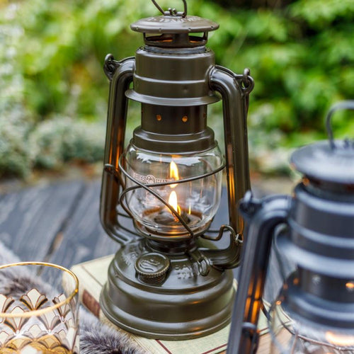 Unique handcrafted dark green galvanized oil lantern with heat-resistant SUPRAX globe softly illuminated on a rustic wooden surface, ideal for Lamps & Lighting, Camping, and Emergency Supplies collections.