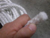 Close-up of a hand holding thick white fiberglass wick material used for lamps, with a coil of similar wicking in the background, featured in lamps and lighting parts and accessories.