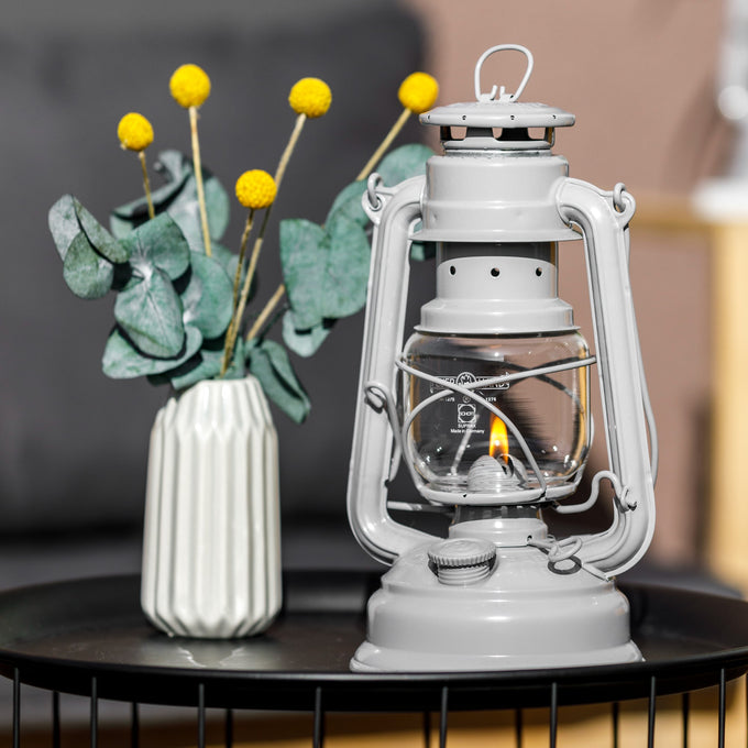 Handcrafted light gray galvanized oil lantern with thermal heat-resistant SUPRAX globe burning softly, displayed beside a vase with yellow billy balls and eucalyptus, perfect for Lamps & Lighting, Camping, and Emergency Supplies collections.