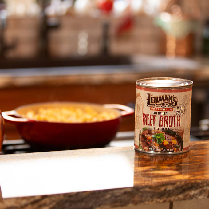 Can of handcrafted Lehman's beef broth placed on a rustic kitchen counter with a red pot simmering in the background, ideal for Farm, Garden & Tool, Kitchen & Food, Emergency Supplies, Food, Meats, Best Sellers, and Promo Eligible collections.