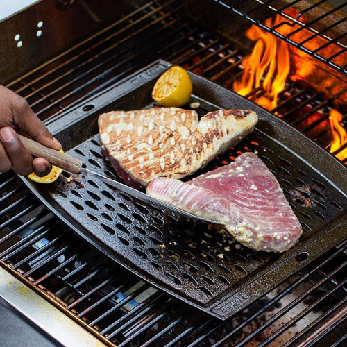 Handcrafted cast iron grill topper pan with perforated surface for enhanced smoky flavor, shown grilling tuna steaks and lemon halves, ideal for Kitchen & Food and Cast Iron collections.