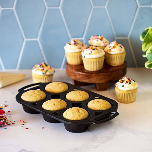 Cast iron muffin pan with six golden muffins cooling on a marble countertop, surrounded by frosted cupcakes with colorful sprinkles, ideal for Kitchen & Food, Cast Iron, Baking Supplies, USA Made, and Best Sellers collections.