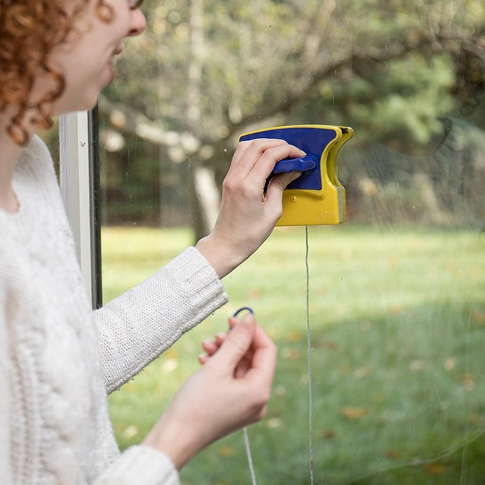 Person using a handcrafted magnetic window cleaner with yellow and blue plastic housing and safety rope, designed for safe and easy window cleaning from inside, featured in Home & Decor and Household Cleaning collections.
