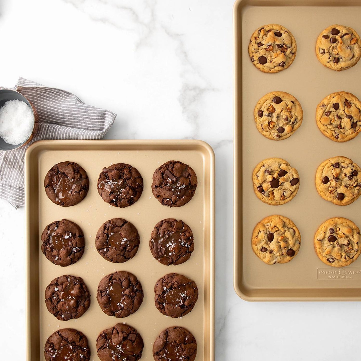 Two gold-toned nonstick half-sheet pans each holding freshly baked chocolate chip cookies on a white marble surface, ideal for Kitchen & Food, Cookware, Baking Supplies, and USA Made collections.