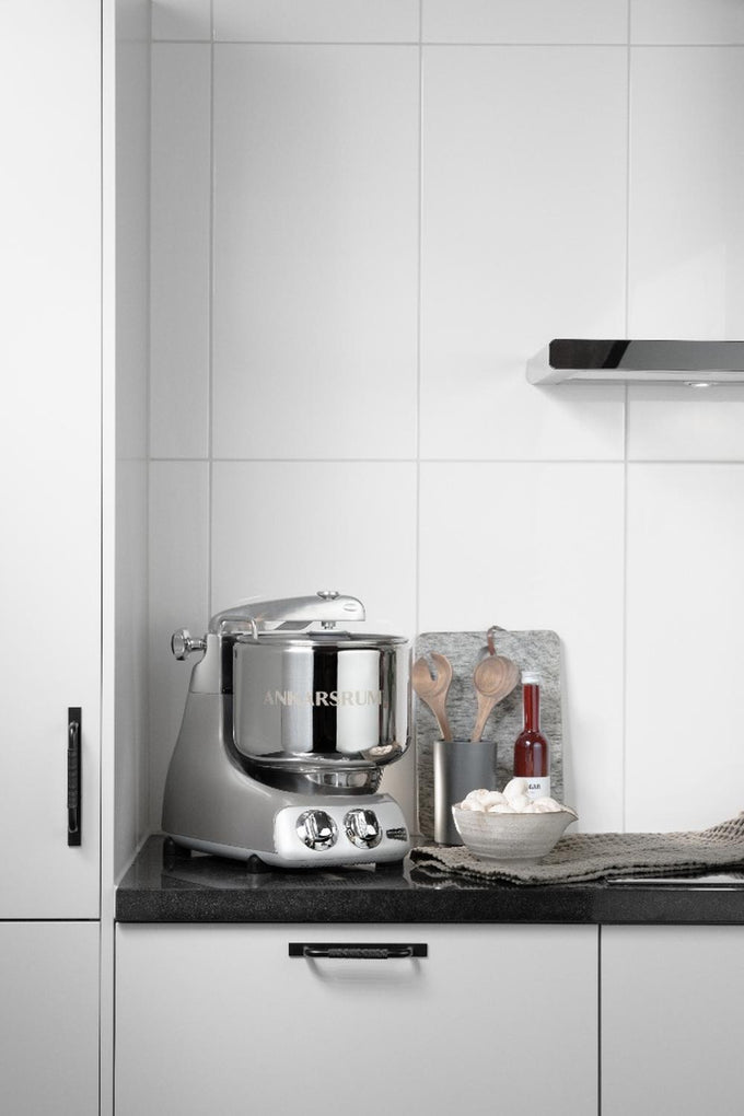 Handcrafted silver stand mixer with polished stainless steel bowl on a black countertop, accompanied by wooden utensils, a red bottle, and a bowl of mushrooms, perfect for Kitchen & Food, Baking Supplies, Cooking and Baking Helpers, and Bread Making collections.