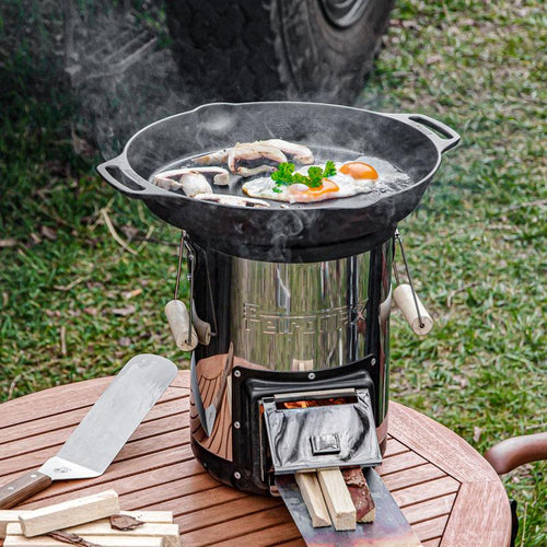 Handcrafted cast iron skillet with two handles cooking eggs and mushrooms on a compact outdoor fire stove, perfect for farm, camping, kitchen, cookware, and cast iron collections.