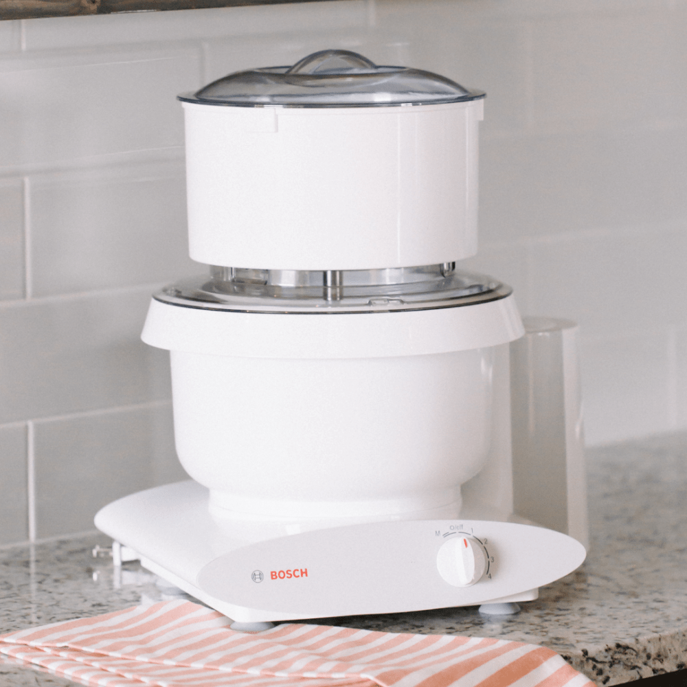 White kitchen appliance featuring a flour sifter attachment with clear lid on a Bosch stand mixer, handcrafted for baking and included in Kitchen & Food and Baking Supplies collections.