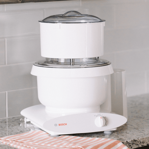 White kitchen appliance featuring a flour sifter attachment with clear lid on a Bosch stand mixer, handcrafted for baking and included in Kitchen & Food and Baking Supplies collections.