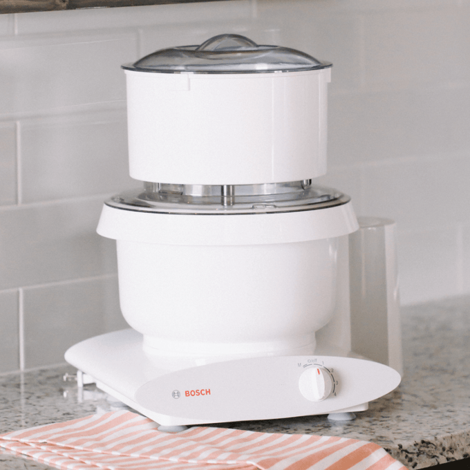 White kitchen appliance featuring a flour sifter attachment with clear lid on a Bosch stand mixer, handcrafted for baking and included in Kitchen & Food and Baking Supplies collections.