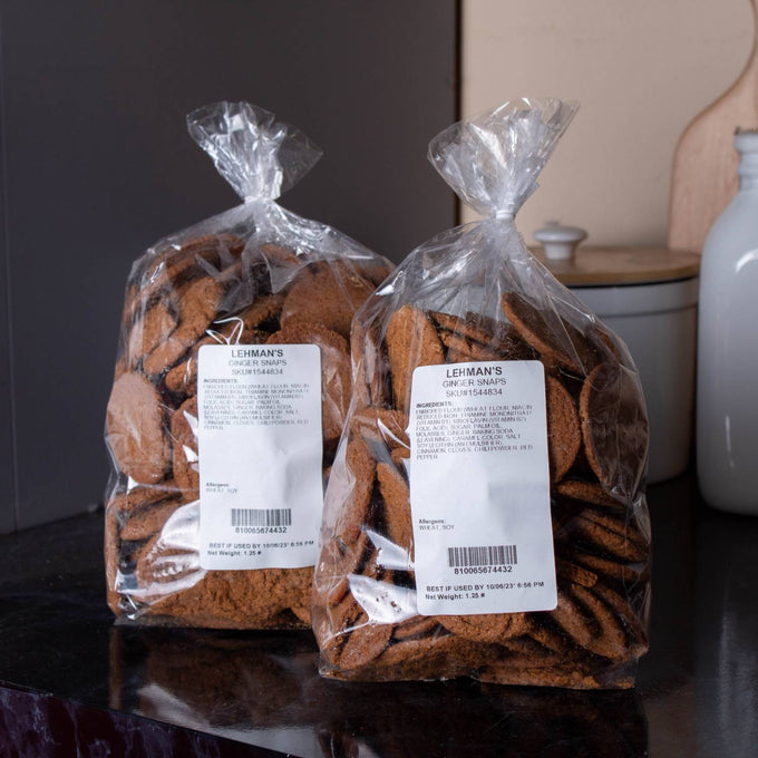 Two clear bags filled with handcrafted ginger snap cookies made in USA, shown on a dark countertop with kitchen items in the background, part of Kitchen & Food, Snacks and Sweets, USA Made, and Best Sellers collections.