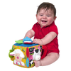 Baby in red outfit playing with colorful fabric musical farmyard cube featuring animal faces, textured details, and interactive sound elements, ideal for indoor play and learning.