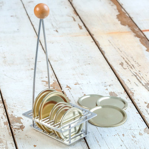 Handcrafted rack with wooden knob handle holds 12 canning lids securely in individual slots, designed for safe steam sterilizing, ideal for kitchen, food preservation, and homesteading collections.