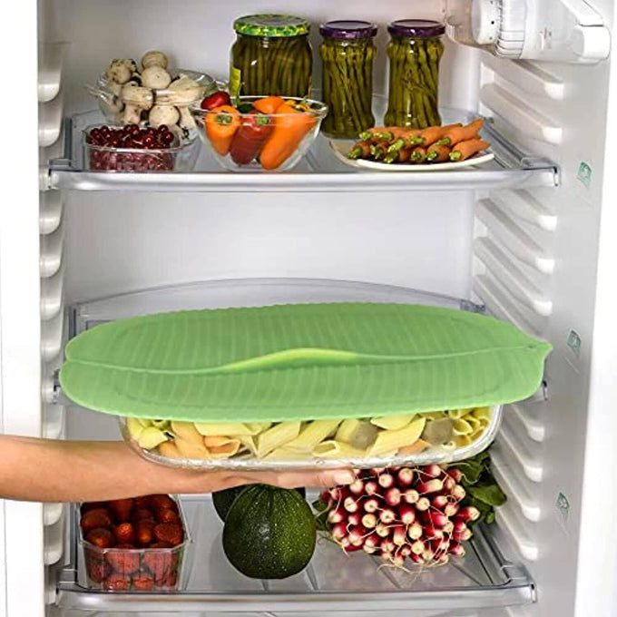 Translucent green silicone bowl cover with a banana leaf design sealing a glass dish inside a refrigerator, featuring durable, food-grade material for Kitchen & Food and Storage collections.