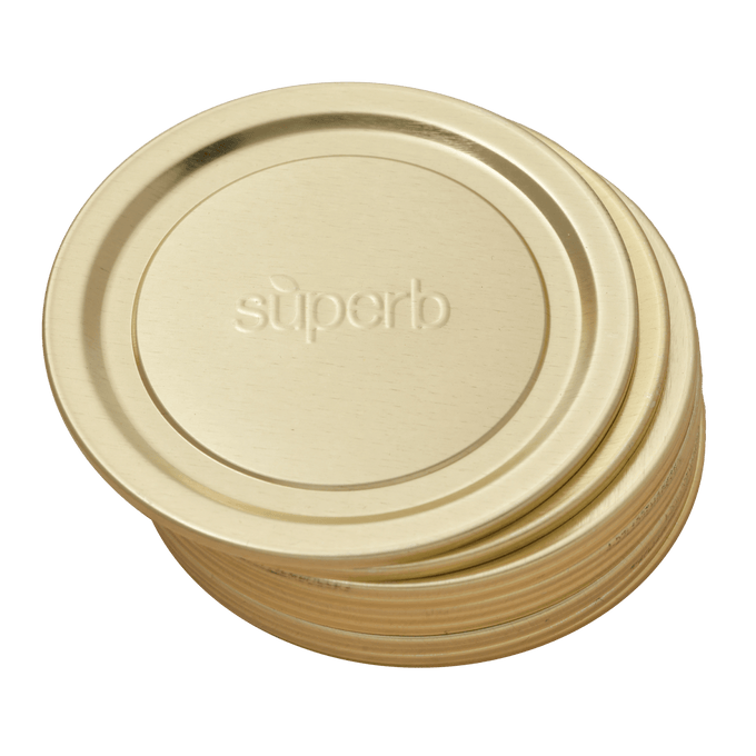 Stack of gold-tone metal regular-mouth canning jar lids embossed with "superb," designed for reliable sealing in food preservation, featured in USA made and kitchen collections.