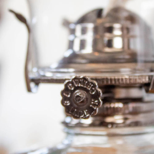 Close-up of a handcrafted metal adjustment knob on a clear glass oil lamp, part of lamps & lighting, oil lamps, table lamps, best sellers, and promo eligible collections.