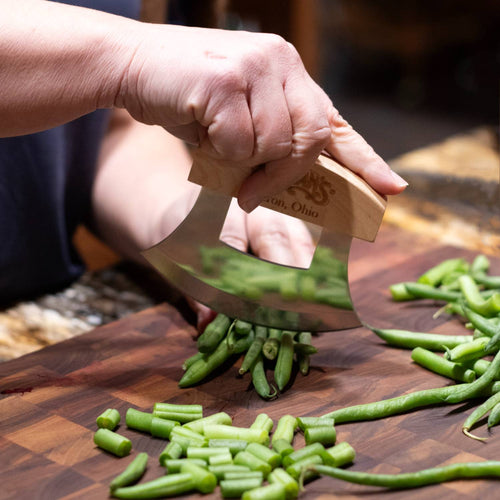 Handcrafted crescent-shaped wooden-handled ulu knife swiftly chopping fresh green beans on a wooden cutting board, ideal for Farm, Garden & Tool, Kitchen & Food, and Food Prep collections.