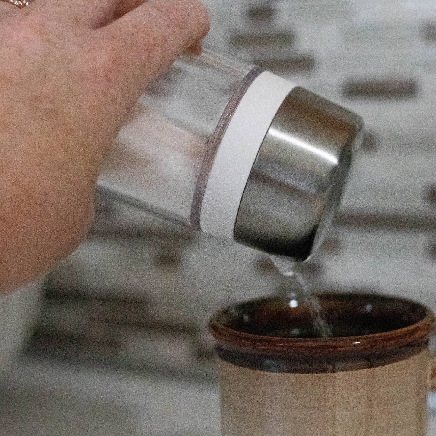 Hand pouring sugar from a clear glass dispenser with stainless steel lid and side spout into a brown ceramic mug, designed to prevent clumping, ideal for Kitchen & Food, Kitchen Gadgets, Storage and Serving, Best Sellers, and Promo Eligible collections.