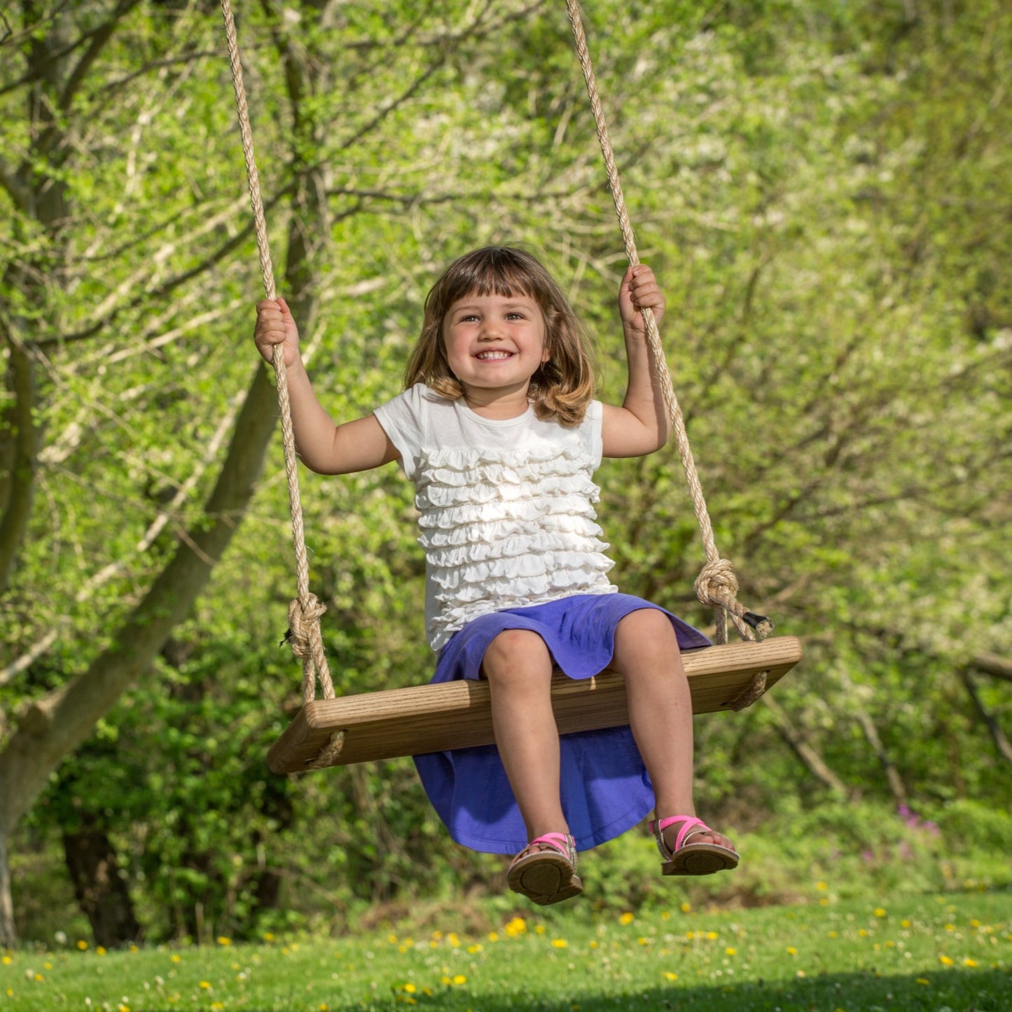 Young girl joyfully swinging on a handcrafted wooden rectangle-style tree swing in a sunny outdoor setting, part of USA Made and Children's Toys collections.