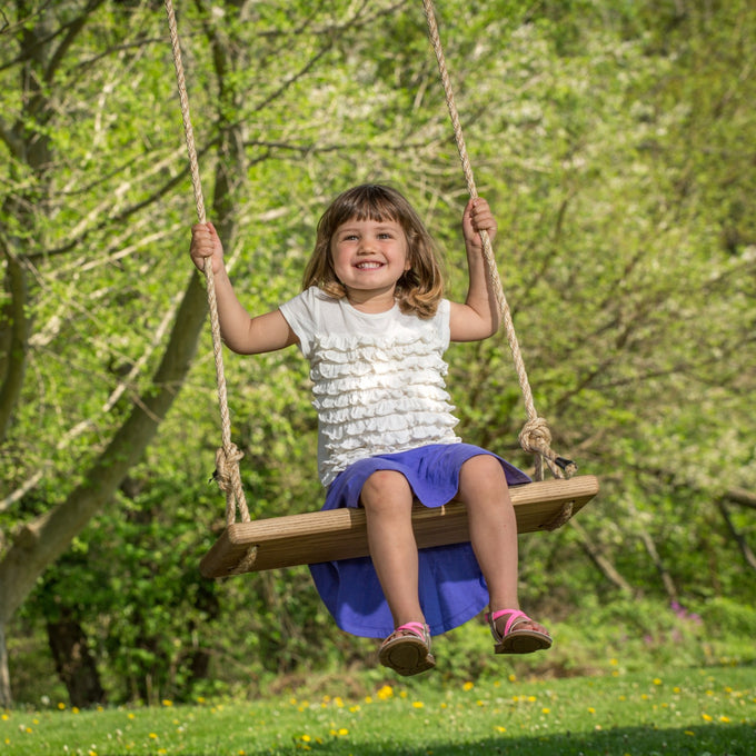 Young girl joyfully swinging on a handcrafted wooden rectangle-style tree swing in a sunny outdoor setting, part of USA Made and Children's Toys collections.