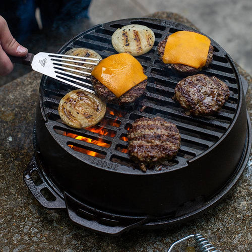 Cast iron portable round grill with burger patties topped with melted cheddar cheese and sliced onions cooking over an open flame, ideal for camping and outdoor grilling.