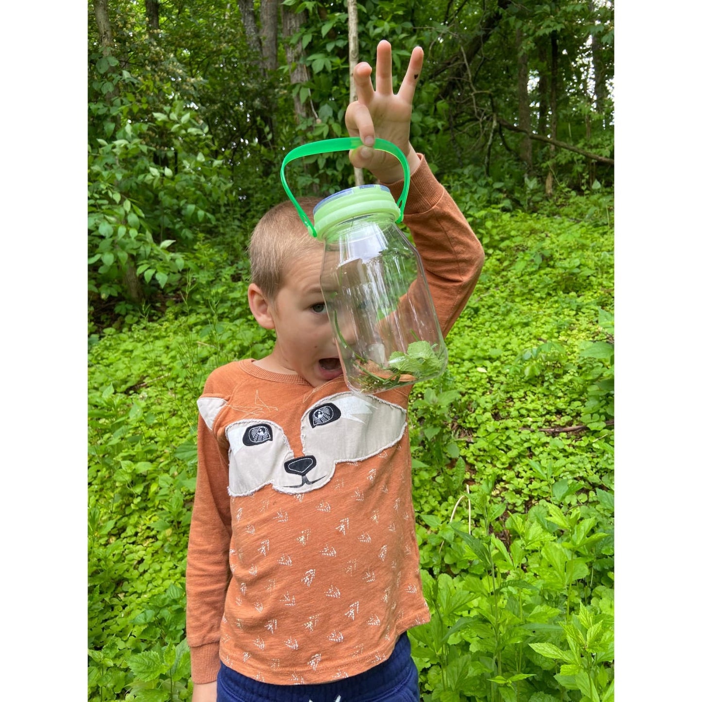 Child outdoors holding a handcrafted, clear plastic bug catcher with green glow-in-the-dark lid and handle, exploring nature in a USA made outdoor play toy from children's collection.