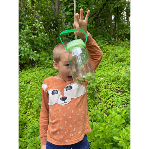 Child outdoors holding a handcrafted, clear plastic bug catcher with green glow-in-the-dark lid and handle, exploring nature in a USA made outdoor play toy from children's collection.