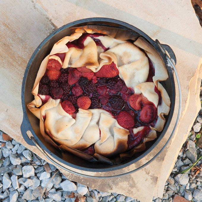 Heavy-duty cast iron camp Dutch oven with built-in legs baking a rustic mixed berry cobbler, perfect for outdoor cooking; featured in Farm, Garden & Tool, Camping, Cast Iron, USA Made, Best Sellers, and Promo Eligible collections.