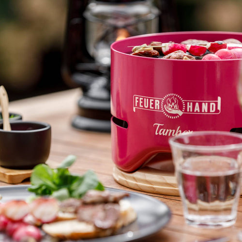 Handcrafted pink tabletop charcoal grill with skewers cooking over low heat, set on a wooden table with glassware and outdoor dining accents, perfect for Farm, Garden & Tool, Camping, and Grilling collections.