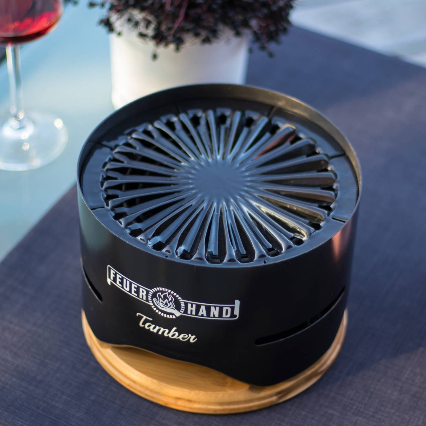 Compact black tabletop charcoal grill with a radial vent pattern and wooden base, handcrafted for small outdoor cooking, featured in Farm, Garden & Tool, Camping, and Grilling collections.