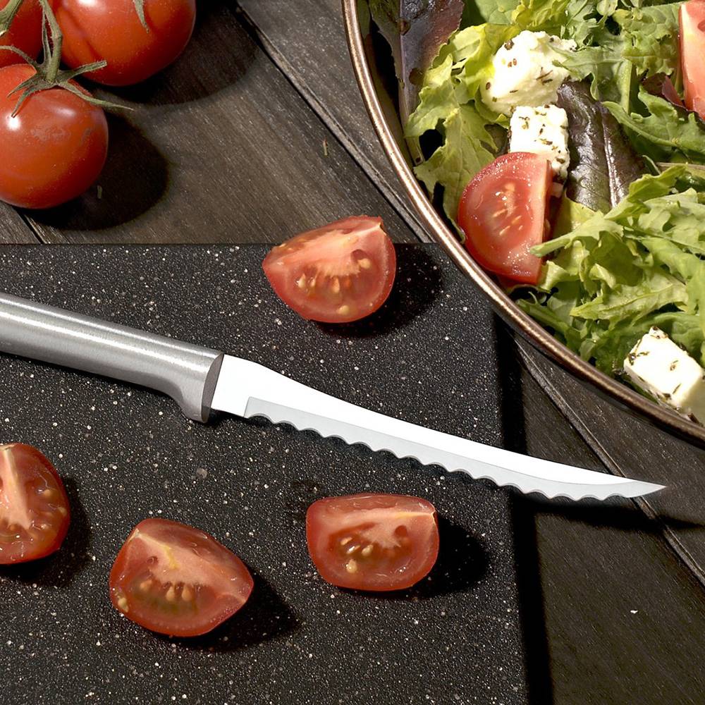Serrated blade tomato slicer with a polished aluminum handle, displayed next to freshly cut tomato wedges and a bowl of salad with leafy greens and feta, handcrafted in USA for kitchen and food prep collections.