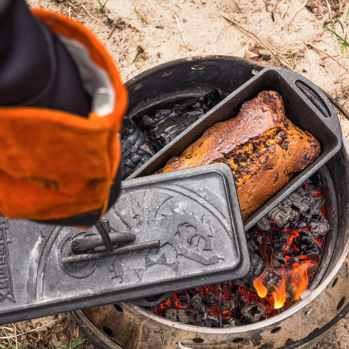 Cast iron loaf pan with embossed lid being removed from hot coals, revealing a freshly baked loaf, perfect for Farm, Garden & Tool, Kitchen & Food, Camping, and Cookware collections.