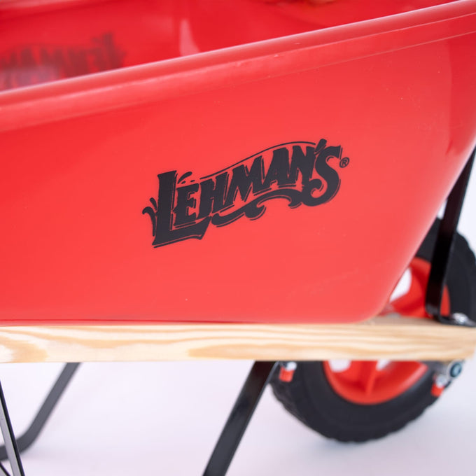 Close-up of a bright red handcrafted kids wheelbarrow with wooden handles and a black Lehman’s logo, designed for outdoor play and garden activities in children’s toy collections.