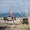 Stainless steel wind-protected enclosure set up on a sandy beach with flames rising, designed to shield fire bowls and Dutch ovens, ideal for Farm, Garden & Tool, Camping, and Best Sellers collections.