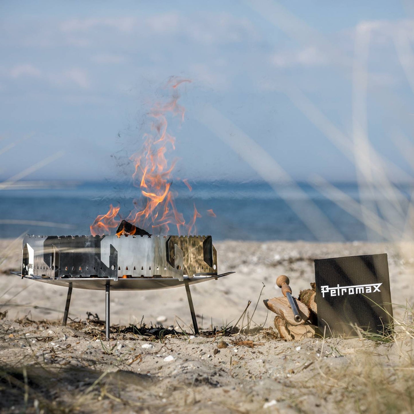 Stainless steel wind-protected enclosure set up on a sandy beach with flames rising, designed to shield fire bowls and Dutch ovens, ideal for Farm, Garden & Tool, Camping, and Best Sellers collections.