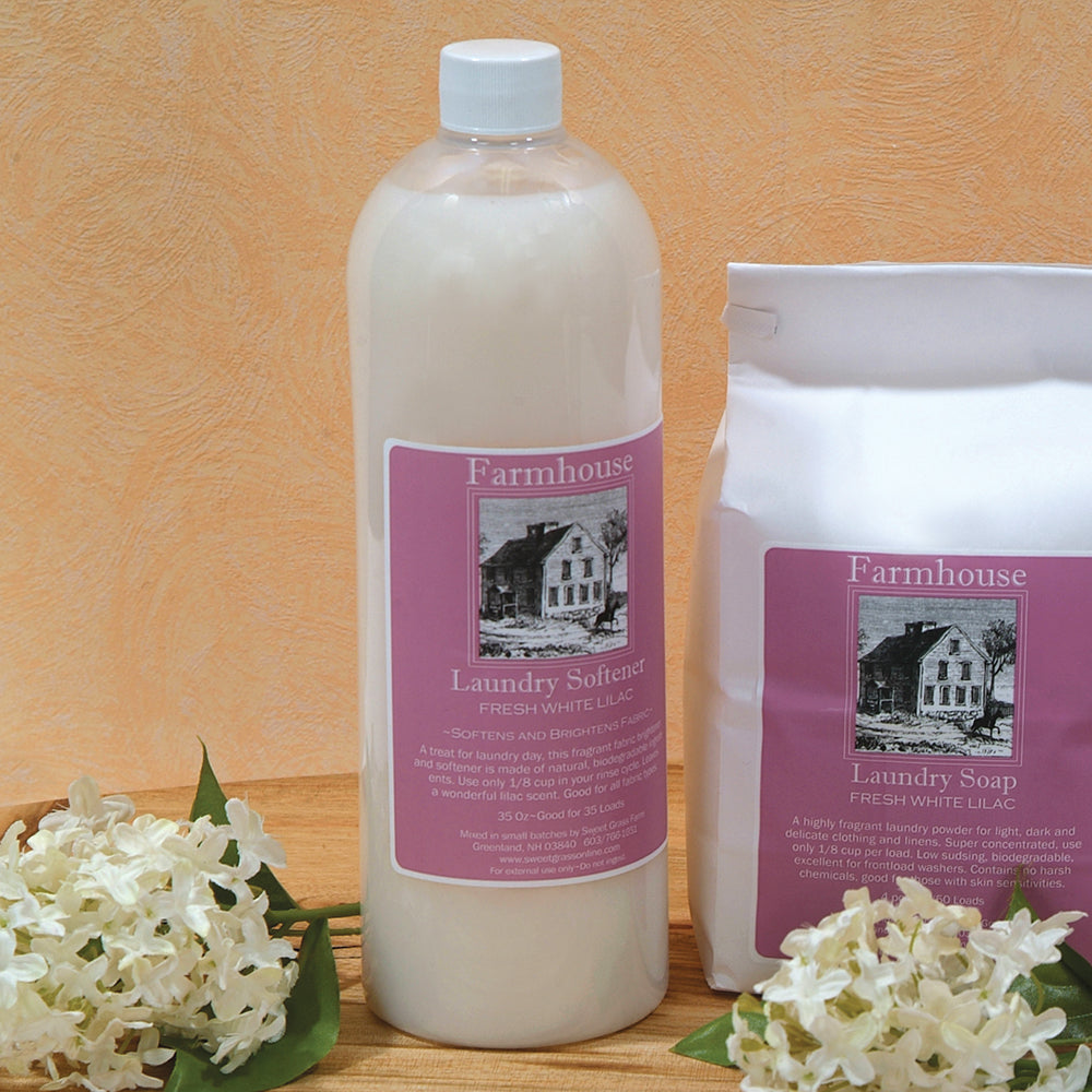 Handcrafted bottle of Farmhouse fabric softener with fresh white lilac scent, alongside matching laundry soap, displayed with white flowers for Home & Decor, Laundry Supplies, USA Made, and Best Sellers collections.