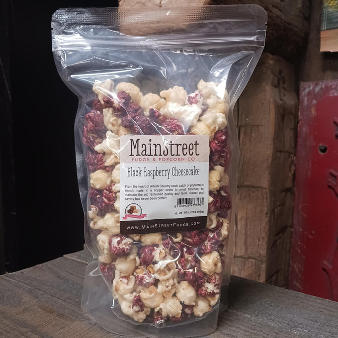 Clear resealable bag of handcrafted Amish-made popcorn in black raspberry cheesecake flavor with a mix of white and deep raspberry-coated pieces, featured in Kitchen & Food, Food, Snacks and Sweets, Popcorn, USA Made, Best Sellers, Promo Eligible collections.
