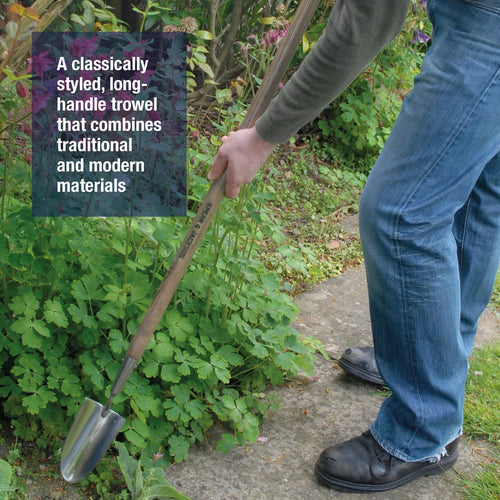 Gardener using a stainless steel long-handled trowel with a weatherproofed wooden handle to turn soil between plants in a garden bed, part of farm and lawncare tools.