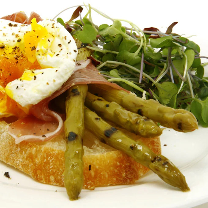 Grilled asparagus spears atop crusty bread with prosciutto and a soft poached egg, garnished with fresh microgreens and cracked black pepper, in Kitchen & Food and Pantry collections.