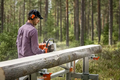 Man using portable chain sawmill to cut a log into lumber outdoors, featuring a sturdy metal frame and designed for ease of use in Farm, Garden & Tool, Wood Cutting and Hauling, and Best Sellers collections.
