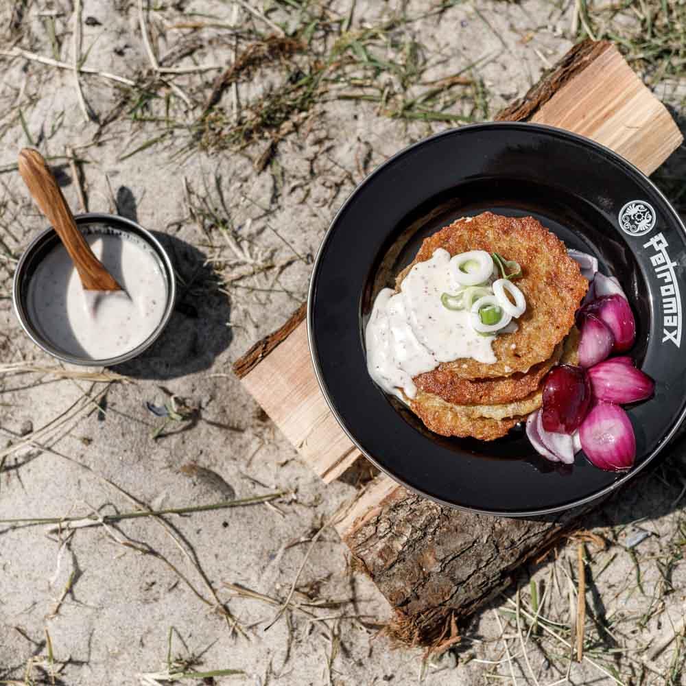 Black enamel Petromax plate with crispy potato pancakes topped with creamy sauce and green onions, served with pickled red onions on a wooden board outdoors, perfect for Camping, Kitchen & Food, Dinnerware, Farm, Garden & Tool, Best Sellers, and Promo Eligible collections.