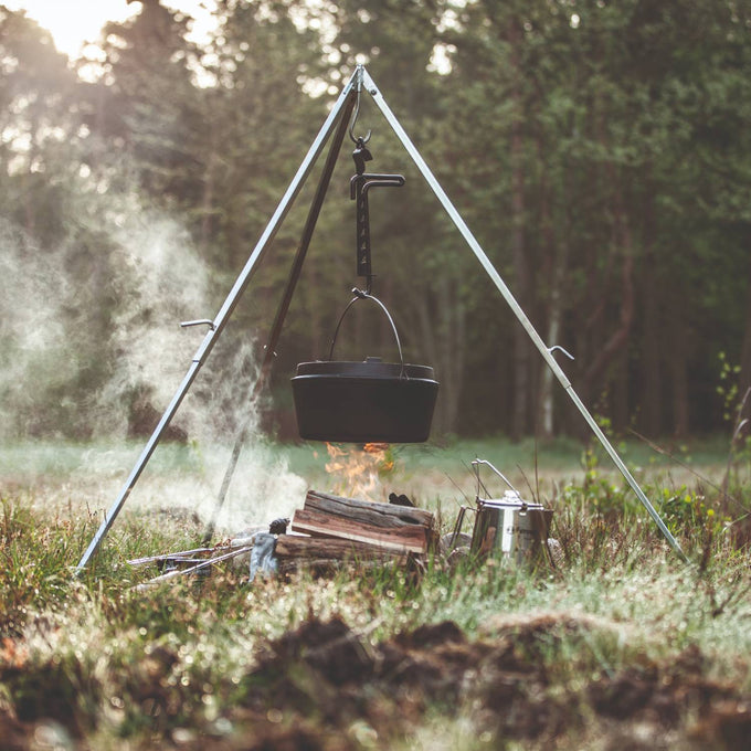 Steel adjustable trammel hook mounted on a tripod suspending a cast iron pot over an open campfire in a forest setting, featured in Farm, Garden & Tool, Camping, Best Sellers, and Promo Eligible collections.
