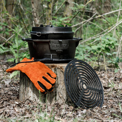 Durable cast iron grill with adjustable grate and sturdy carrying handle, shown outdoors on a tree stump with heat-resistant orange gloves and circular grill grate, ideal for Farm, Garden & Tool, Stoves, Camping, and Grilling collections.